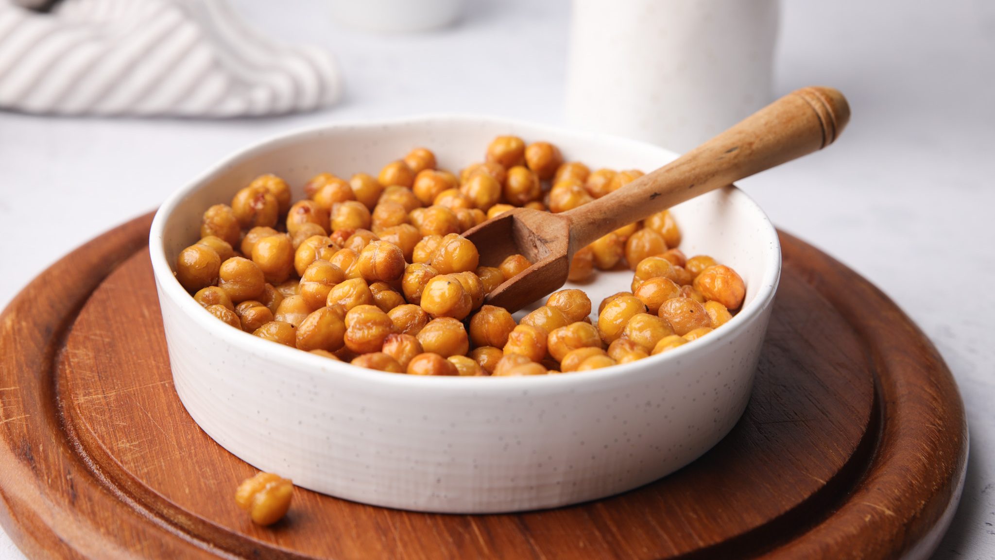 Chickpeas in a white bowl with a wooden scoop.