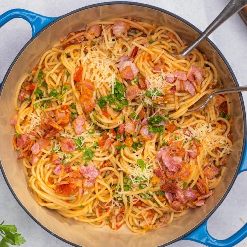 Spaghetti with tomato and bacon in a blue pot, with green herb and grated cheese.