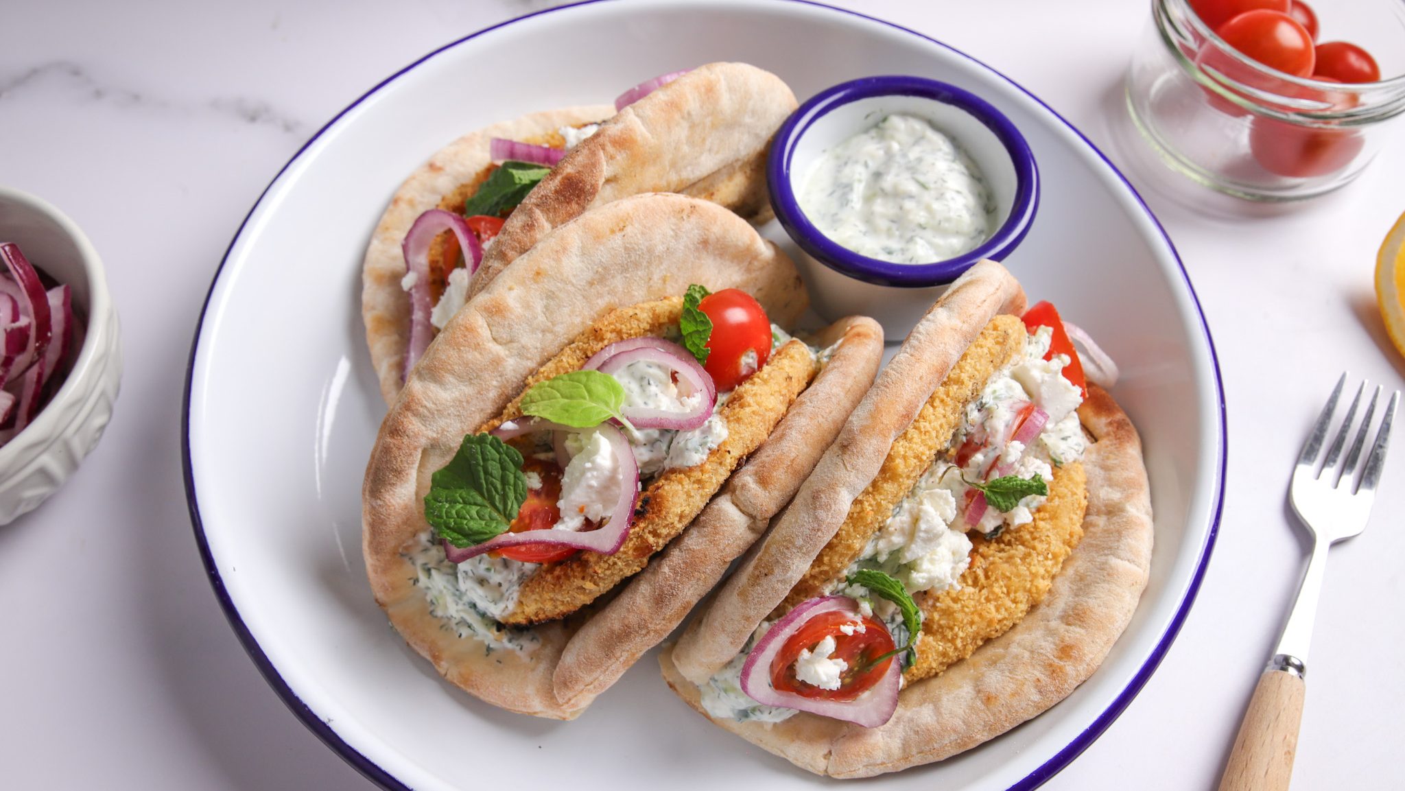 Three pita bread sandwiches on a plate with a pot of white dip.