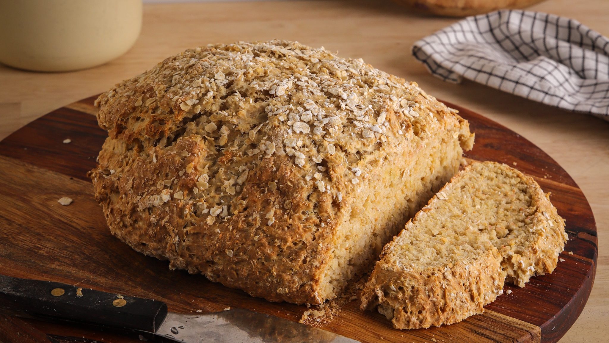 A loaf of bread sliced on wooden board with bread knife.