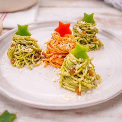 Spaghetti Christmas trees shaped as 4 mounds on a plate, topped with capsicum stars and a sprinkle of grated parmesan.