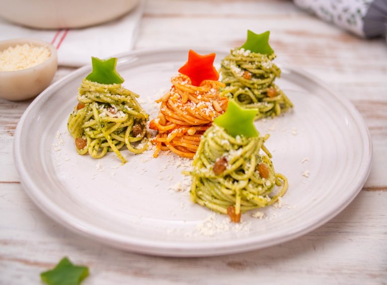 Spaghetti Christmas trees shaped as 4 mounds on a plate, topped with capsicum stars and a sprinkle of grated parmesan.