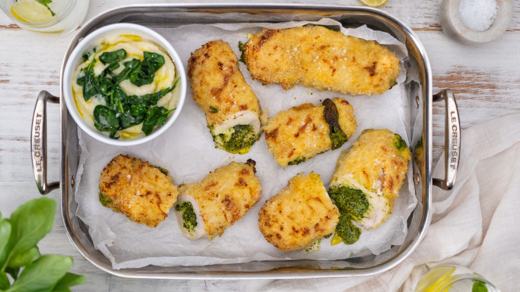 Chicken Kiev rolls with spinach and cheese filling served on a Le Creuset baking tray with a side of potato mash and steamed greens