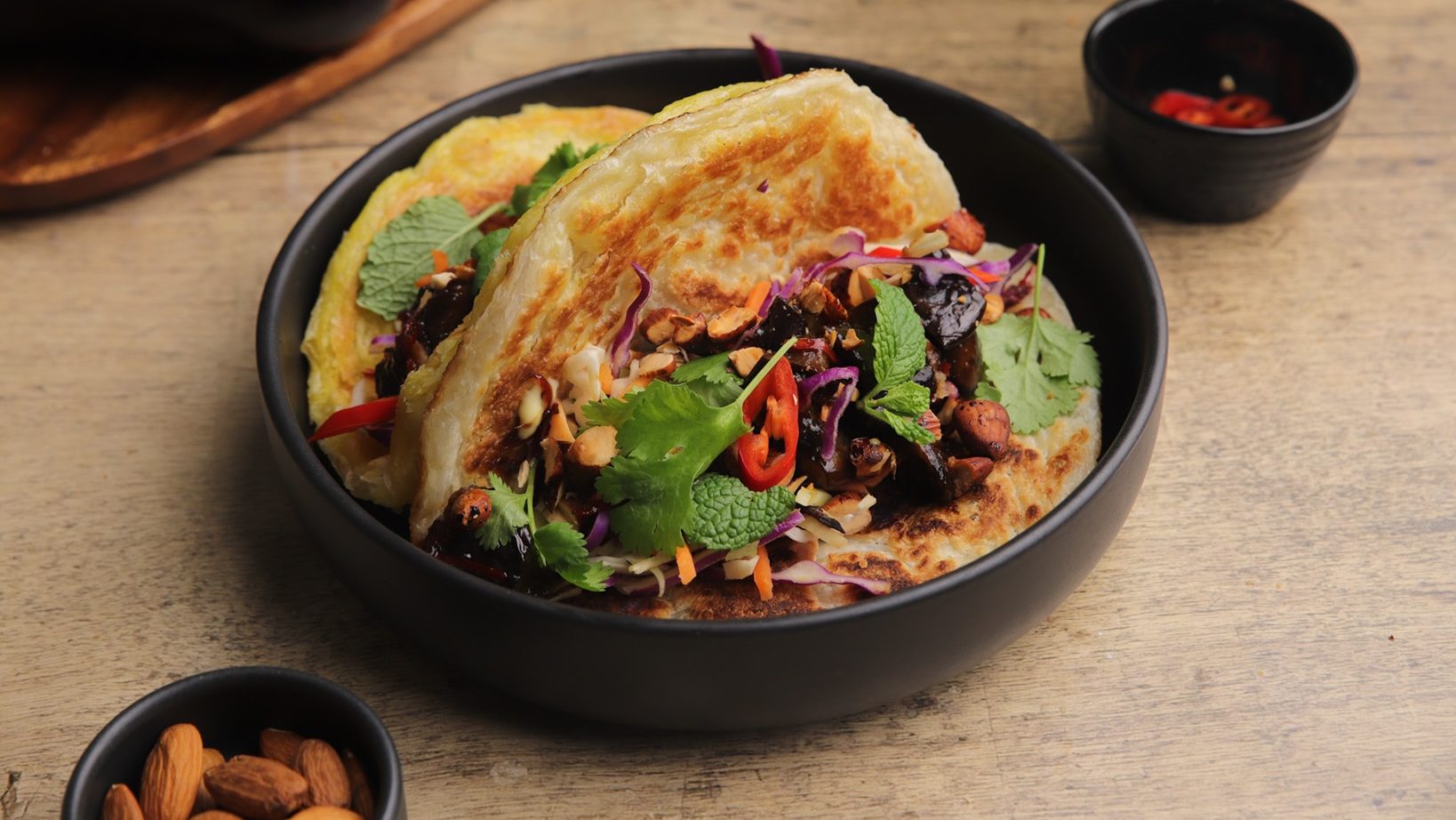 Cooked food on a grilled flat bread in black bowl.