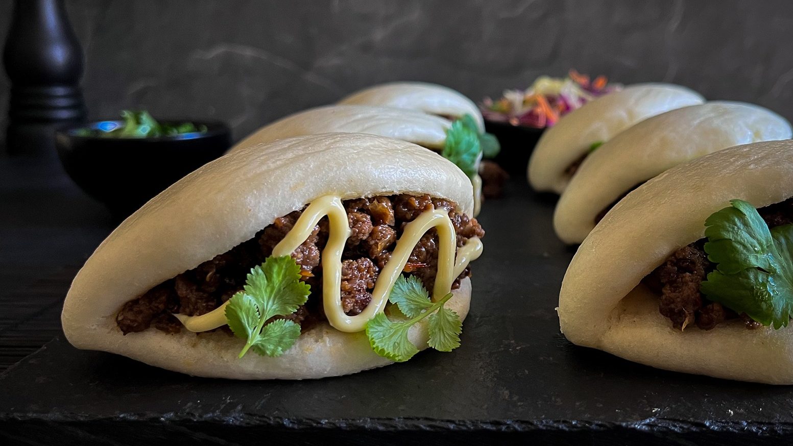 Six bao buns filled with mince, herb and mayo lay flat on black slate.