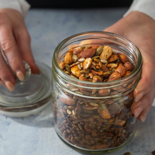 Hands folding a jar of nuts and its lid on table.