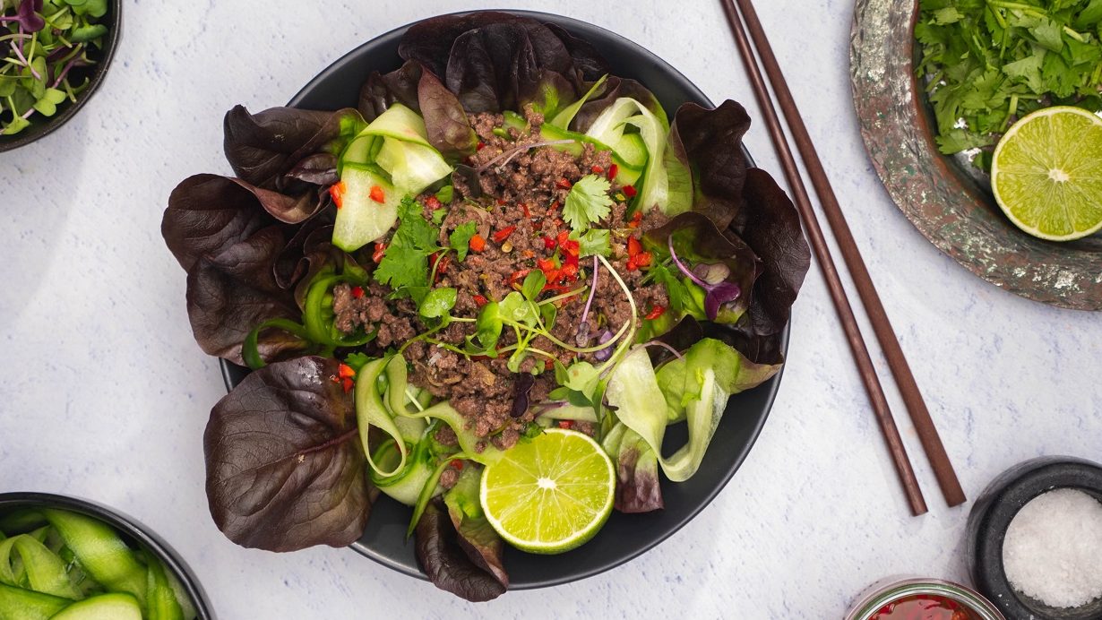 A bowl of salad with green and brown lettuce topped with meat, red chilli and lime. A pair of chopsticks.