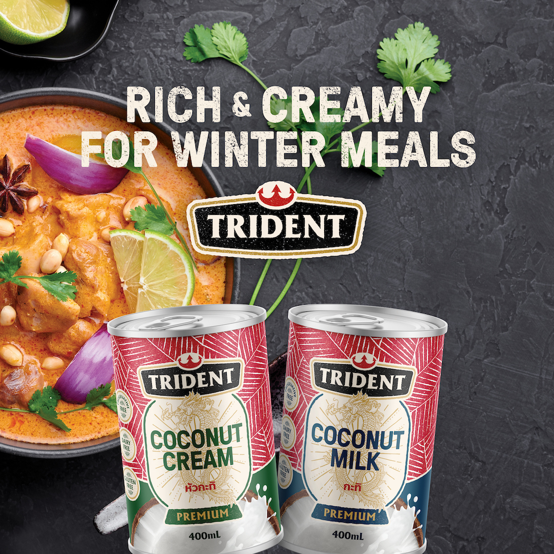 A can each of Trident Coconut Milk and Trident Coconut Cream with a bowl of curry in the background