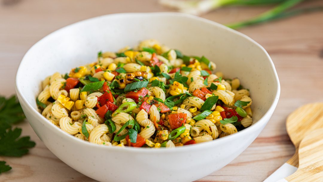 A bowl of pasta salad with red and green food.