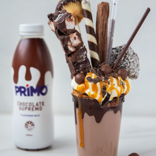 Chocolate freakshake ina glass with wafers and chocolate sticks standing out the top. A chocolate primo behind it on the left.