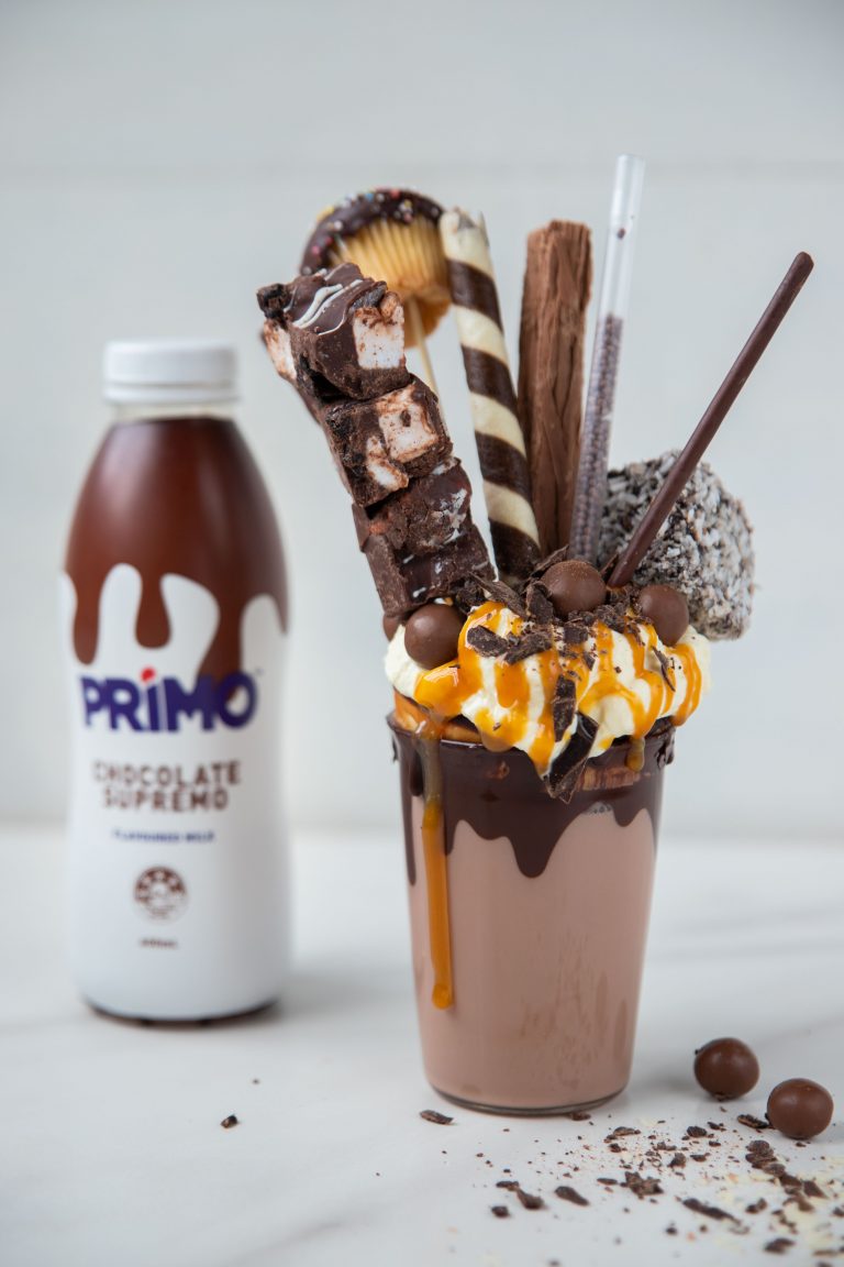 Chocolate freakshake ina glass with wafers and chocolate sticks standing out the top. A chocolate primo behind it on the left.