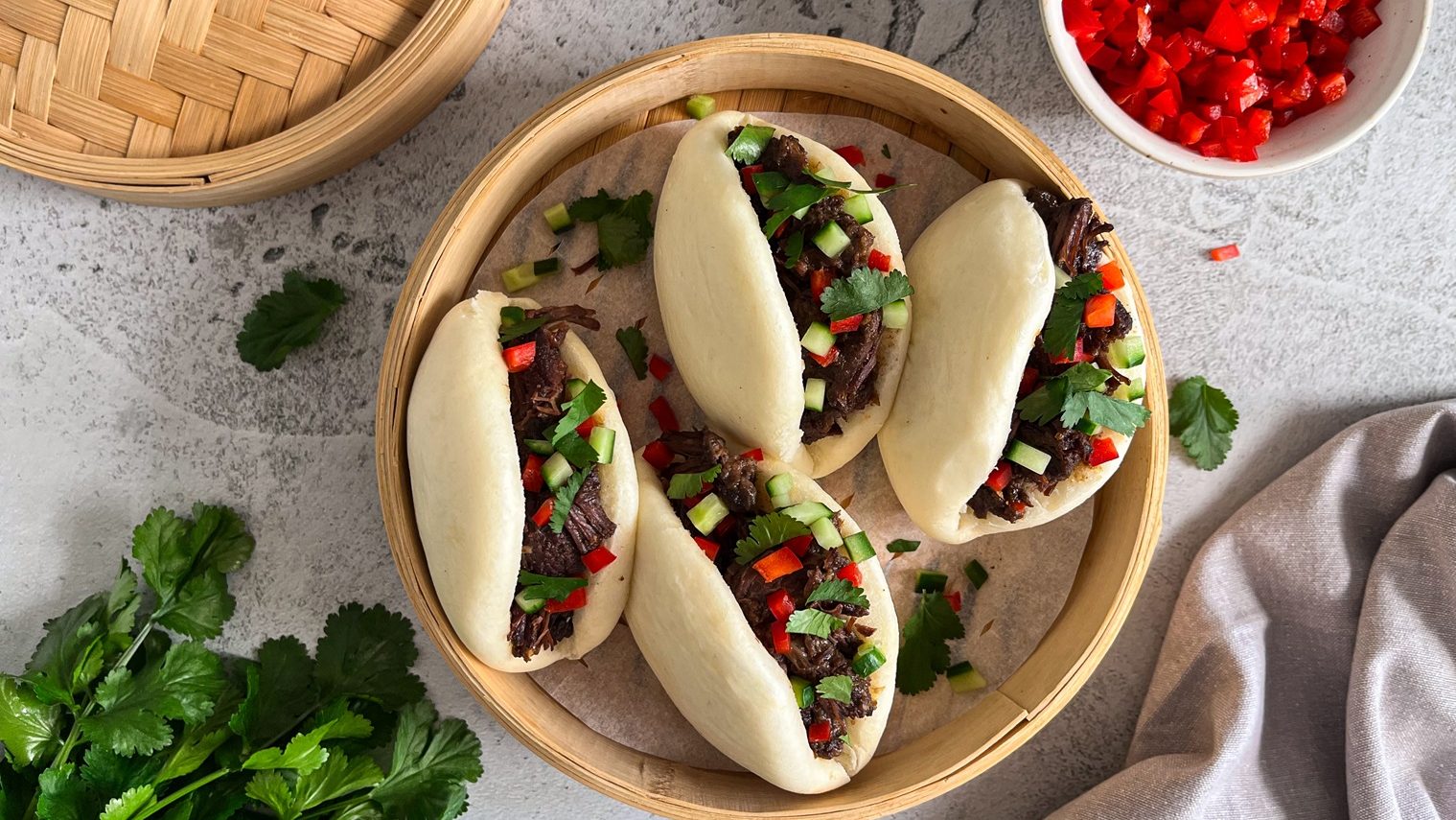 Four meat and colourful vegetables filled bao buns in a bamboo steamer.