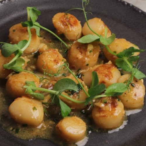 Cooked scallops topped with pea shoots on a black plate.