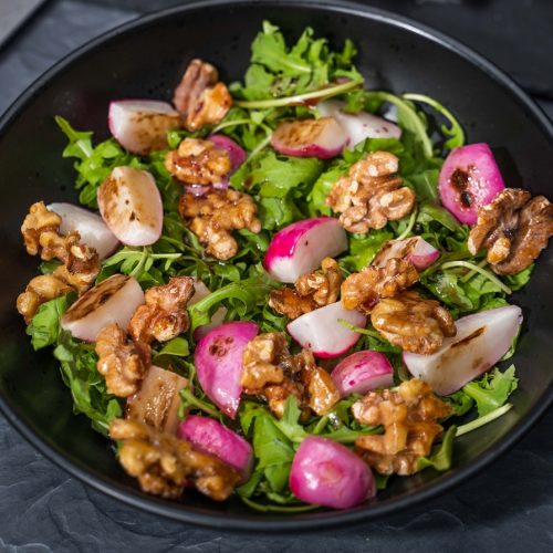 Close up of red radish, walnuts and green salad in a black bowl.