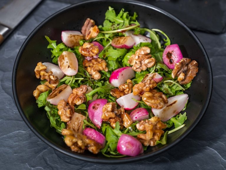 Close up of red radish, walnuts and green salad in a black bowl.