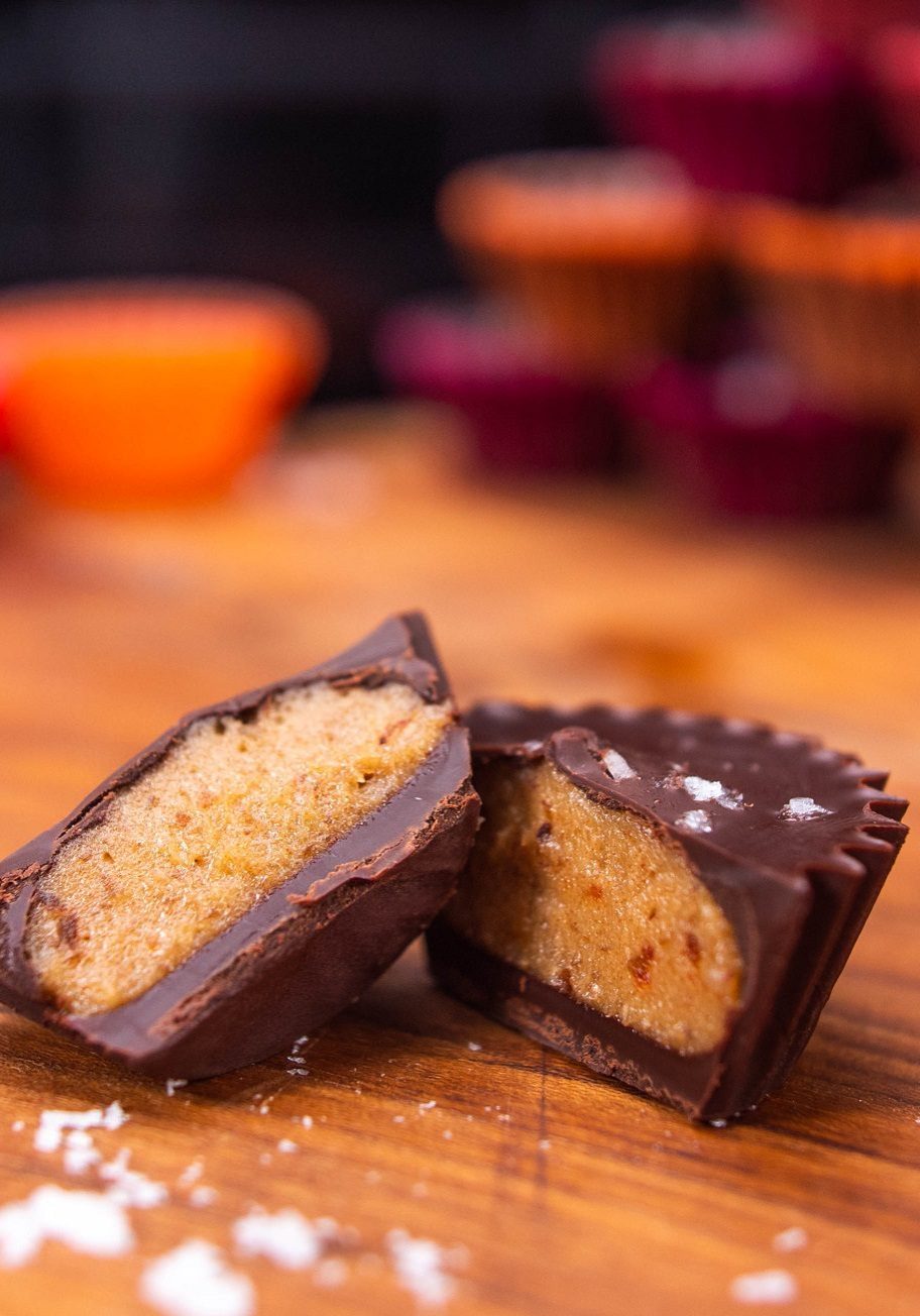 A nut-free peanot butter cup-shaped sweet snack with a chocolate coat, cut in half on a wooden chopping board.