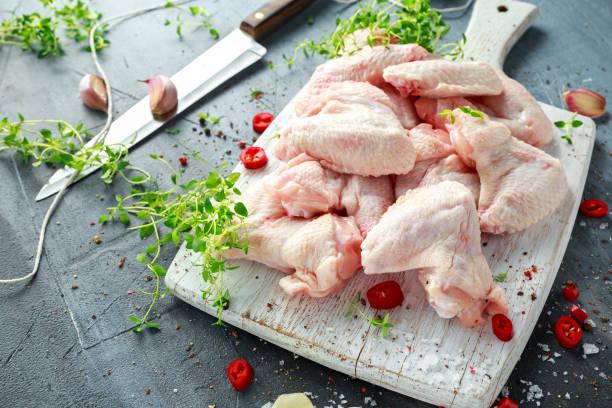 Fresh raw chicken wings on a white cutting board with thyme, chilli, salt, pepper, garlic.