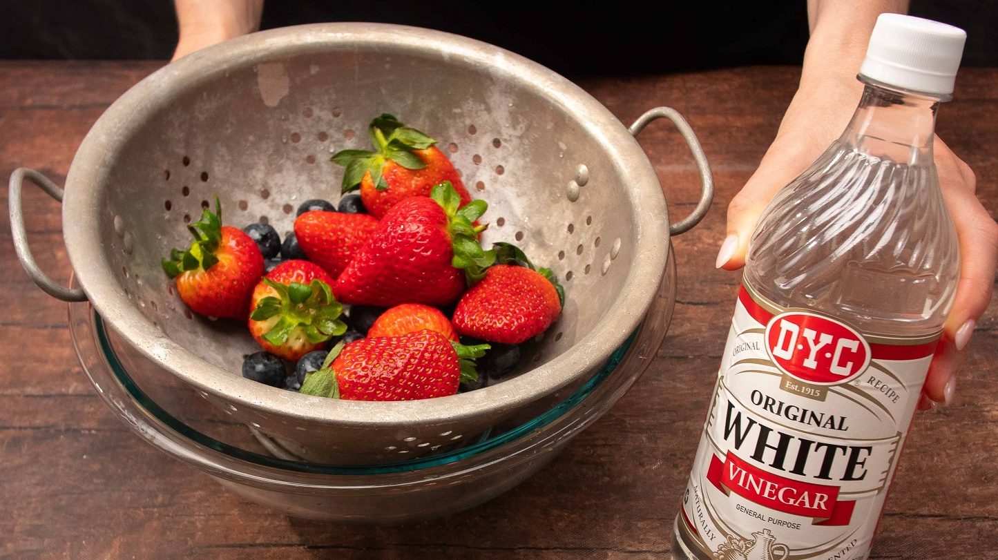 Sieve of strawberries and a bottle of vinegar